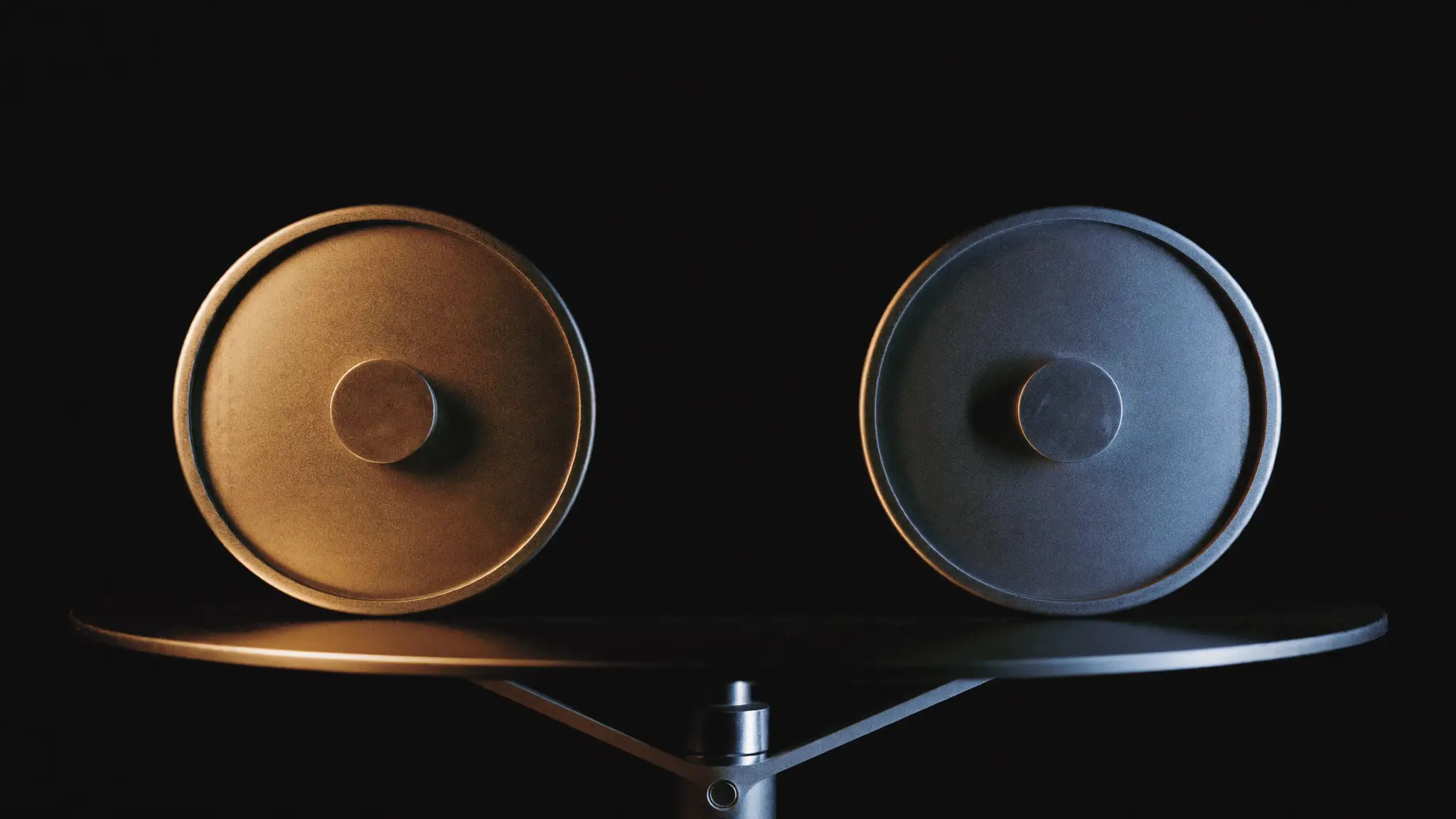 Dois pesos metálicos idênticos em uma balança de precisão perfeitamente nivelada, um iluminado em luz quente e outro em luz fria.
